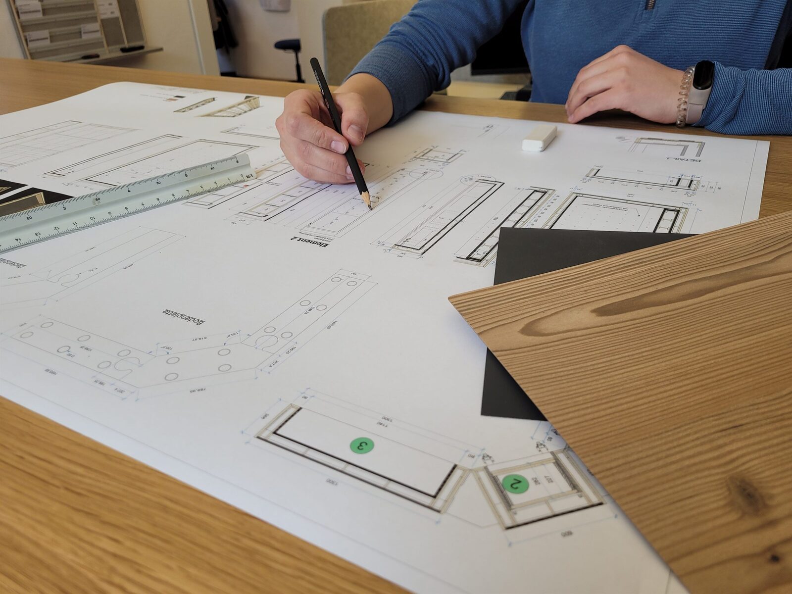 Planung eines Objektausbau-Projekts am Zeichentisch mit Werkplänen und Holzmuster